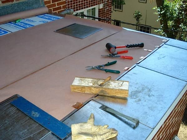 Tin snips, a hammer and metal flashing pieces laid out on a roof deck beside metal panels